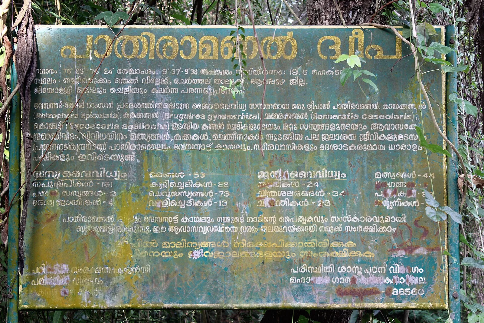 A weathered green government information board on Pathiramanal island, lettered in Malayalam with biodiversity counts