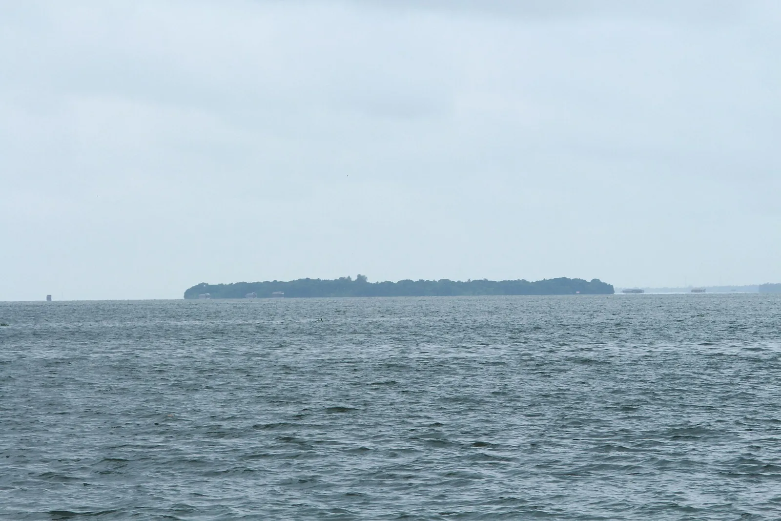 Pathiramanal island seen as a low wooded line across the open water of Vembanad Lake under an overcast sky