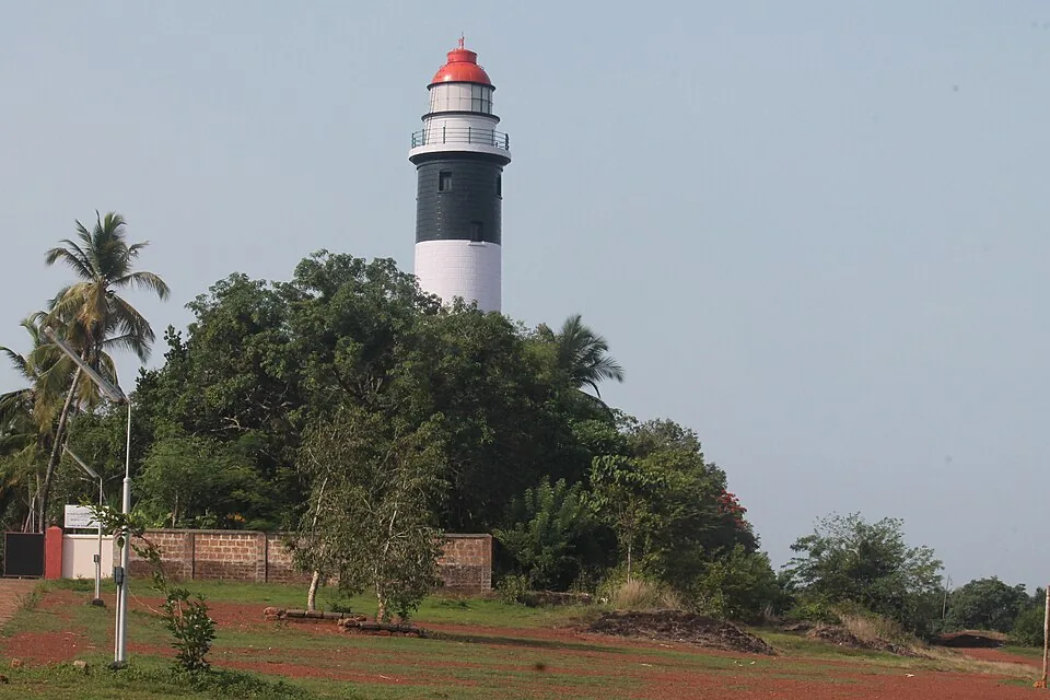 The black-and-white banded tower of the Kadalur Point lighthouse rising above coconut palms and scrub on a red-laterite rise near Thikkoti