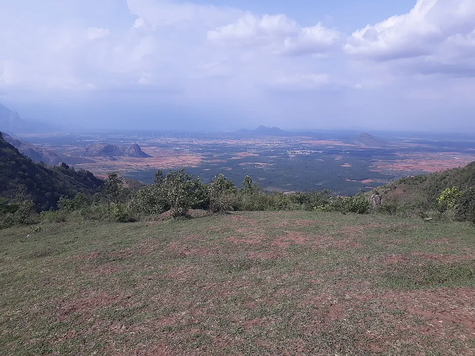 Cropped grass and red earth on the Ramakkalmedu ridge with the farmed Tamil Nadu plain and a distant peak beyond