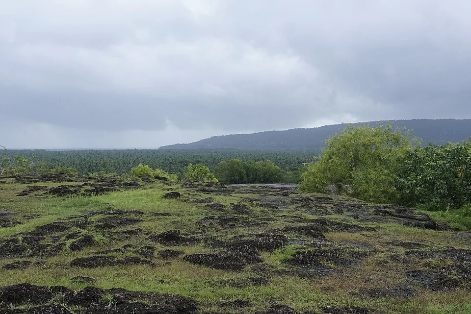 The open laterite surface of Madayipara under cloud, with low scrub and distant hills