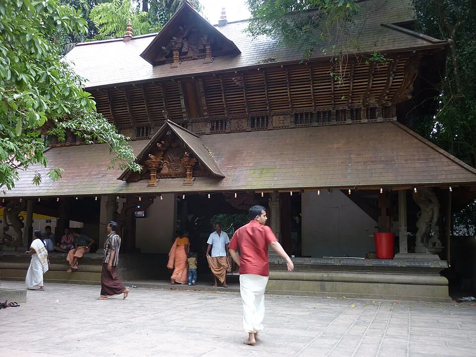 The Mannarasala temple frontage with its deep tiled eaves and carved gable, worshippers crossing the paved forecourt