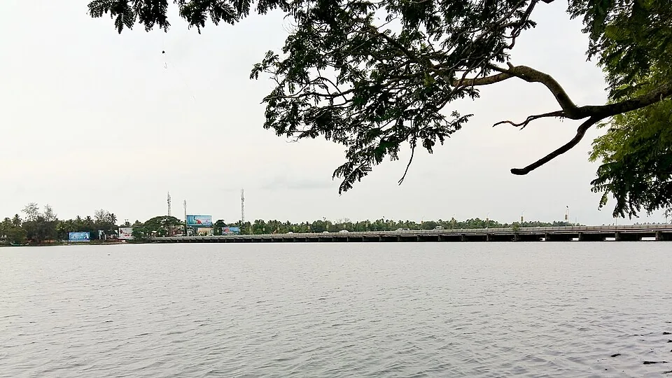 The Thottappally spillway seen across the water, its shutter line running the full width of the frame beneath a pale sky