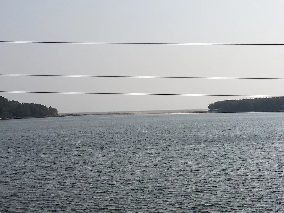 Looking west down the Thottappally channel towards the Arabian Sea, with a continuous sand bar closing the mouth across the frame