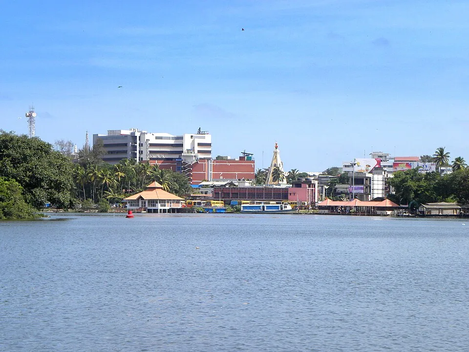 Ashtamudi Lake in the foreground with the low buildings and palms of Kollam town along the far shore under a blue sky