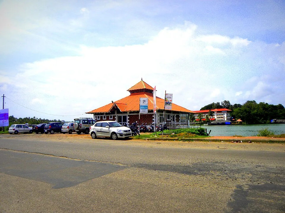 A red-roofed waterfront terminal building with parked vehicles and coconut palms at Kollam, the gateway to the backwaters