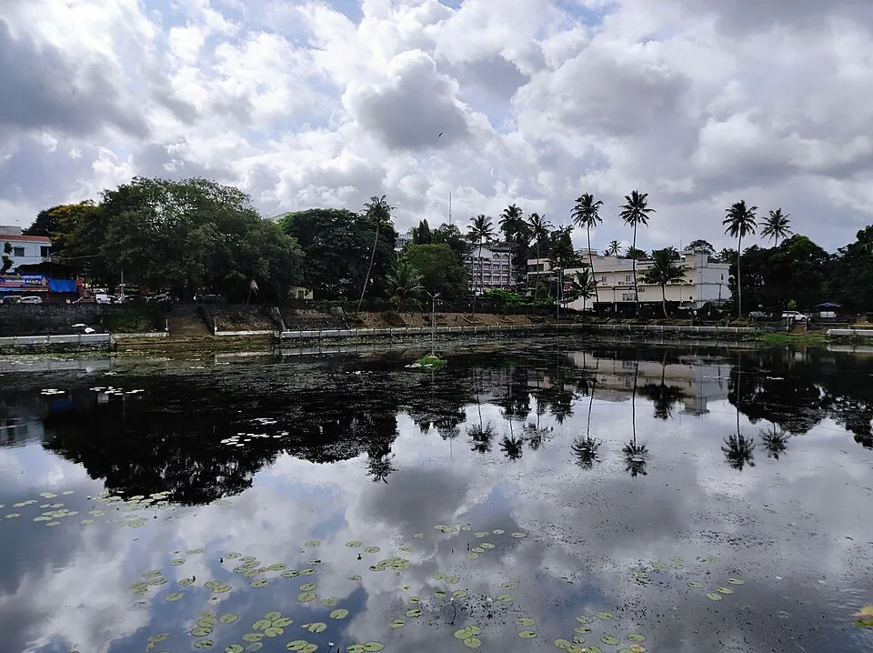 The temple tank at Kottarakkara, a broad sheet of still water edged with laterite steps and retaining walls, with the tiled temple roofs and trees behind it
