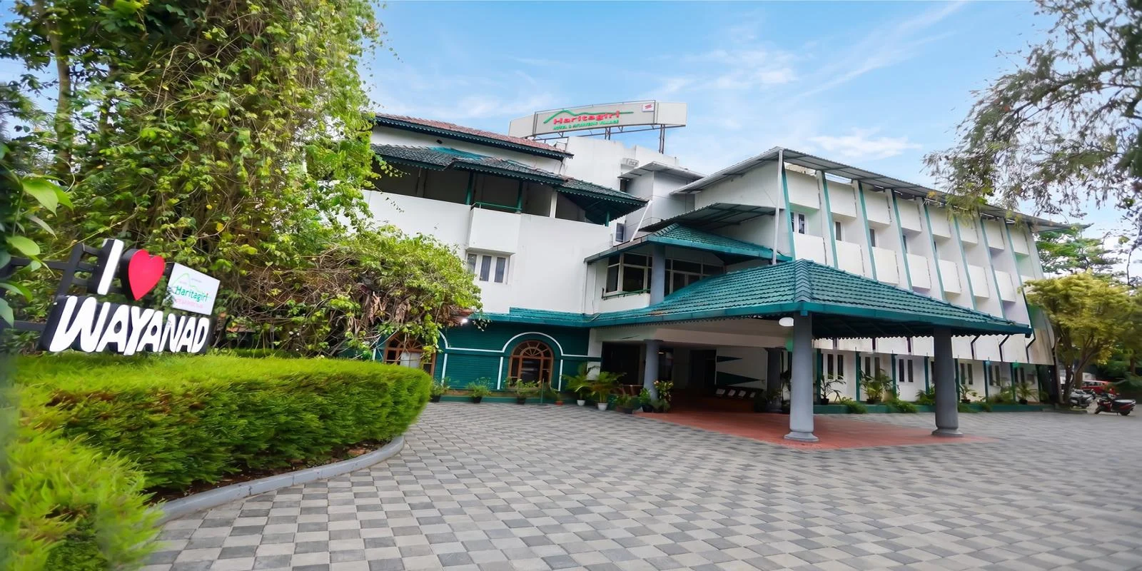Haritagiri’s white hotel building has green roofs, a covered entrance and a paved forecourt beside garden trees.