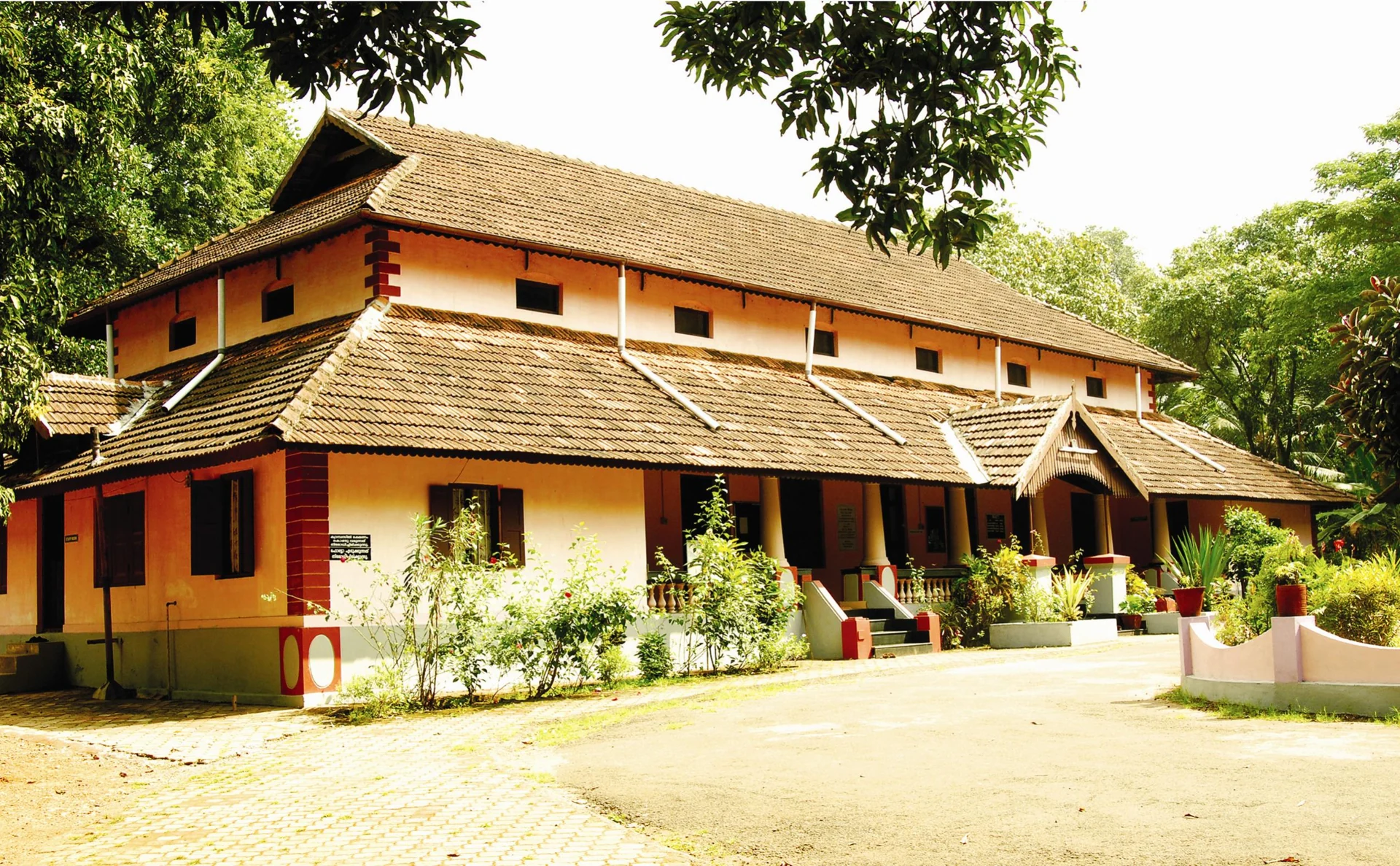 The older Kalamandalam Nila-campus building has ochre walls, dark windows, tiled roofs and steps at its central entrance.
