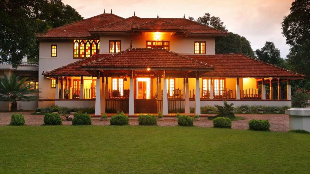 Planters Retreat’s white house has red tiled roofs, a deep veranda and illuminated windows facing a lawn.