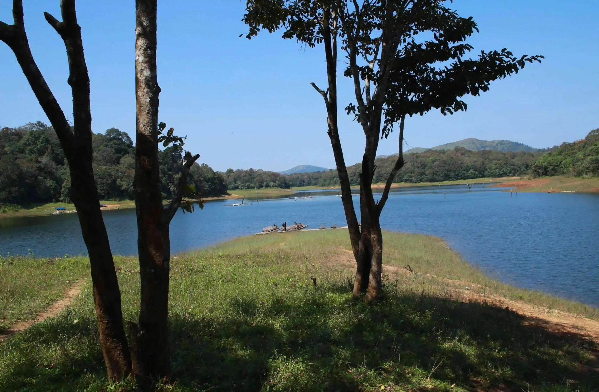 Blue lake water surrounds a grassy, wooded peninsula, with small rafts near the shore.