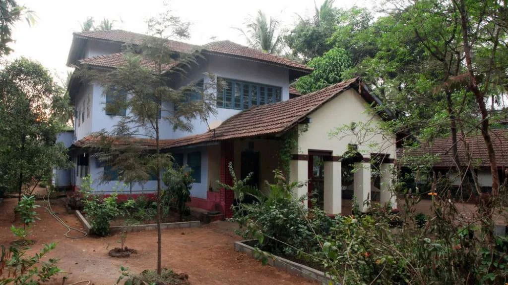 Puthiya Kovilakam’s tiled-roof house has pale blue walls, a covered entrance and trees around an earthen courtyard.