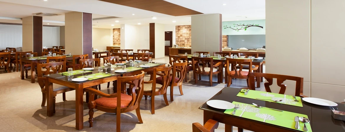 Wooden dining tables set with green placemats inside Sterling Thekkady’s restaurant.