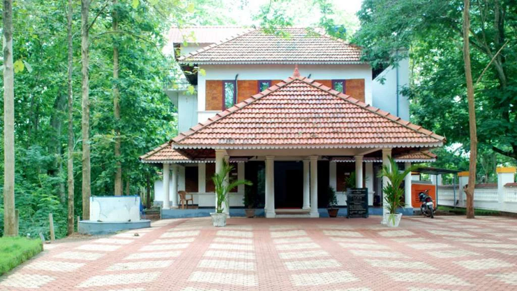 Tamarind Nilambur’s tiled entrance roof faces a red-and-white paved forecourt surrounded by trees.