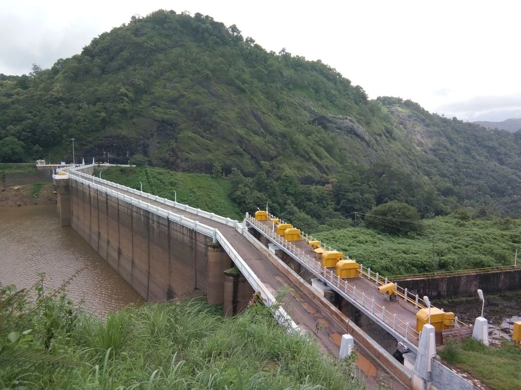 Ponmudi Dam’s exposed reservoir face and yellow gate equipment beneath a green rocky hill