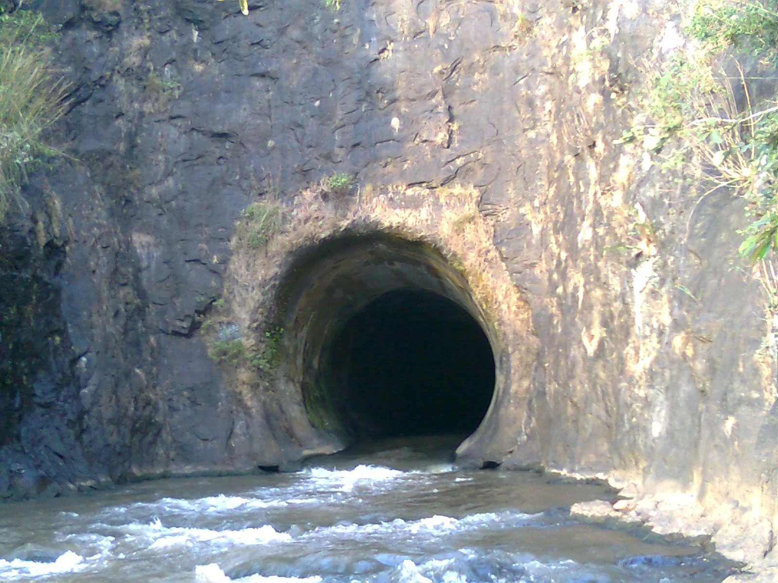 Water emerges from Anchuruli’s circular tunnel outlet over dark rock