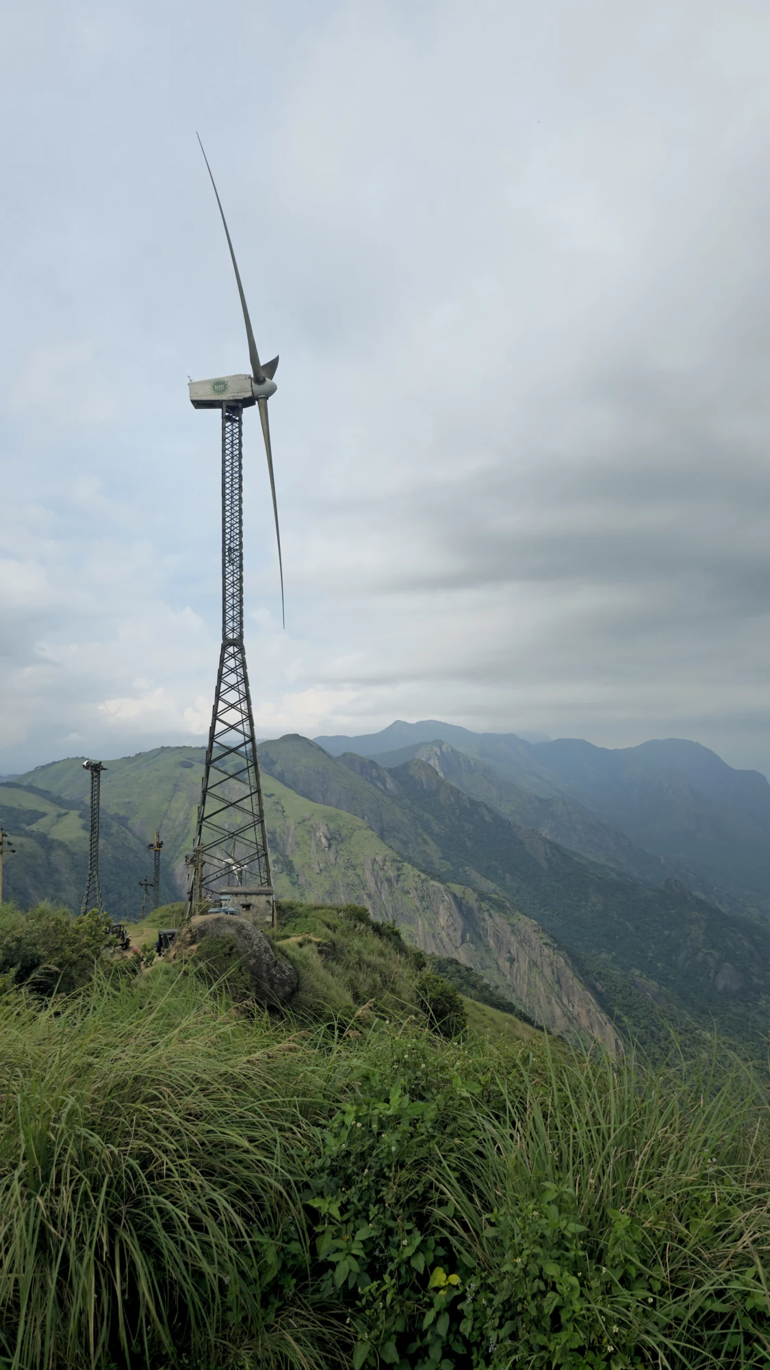 Lattice-tower wind turbine above the grassy Chathurangapara ridge and steep green rock slopes