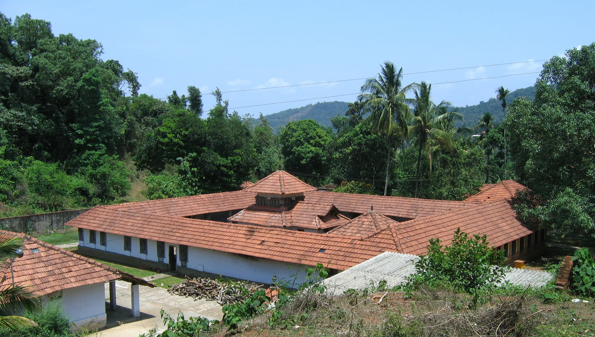 An elevated view shows Thrissilery’s long tiled enclosure roofs, a smaller roof within the court and stored firewood in the foreground.