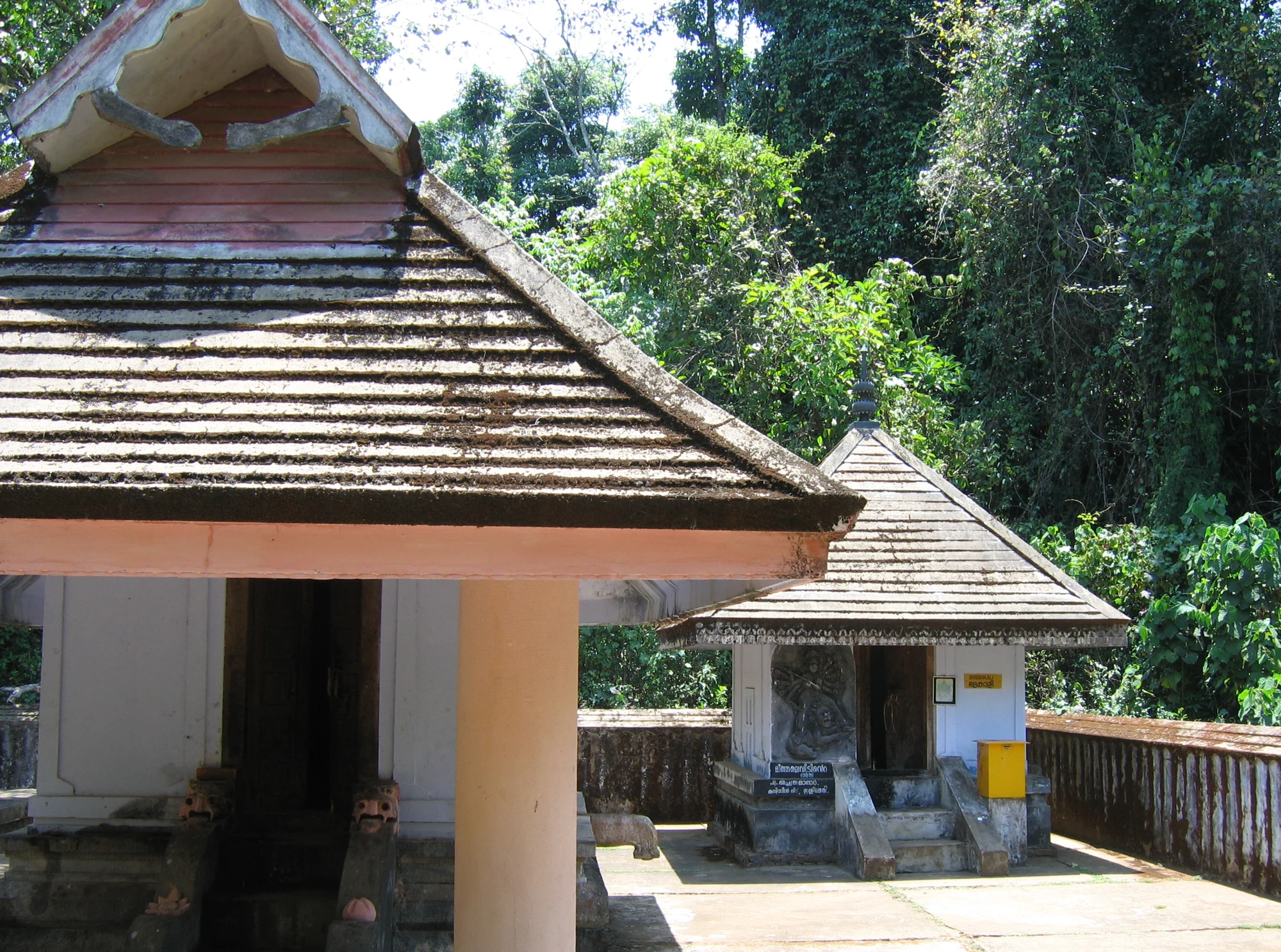 Two small tiled-roof shrines stand beside a white relief-decorated wall in Thrissilery’s courtyard.