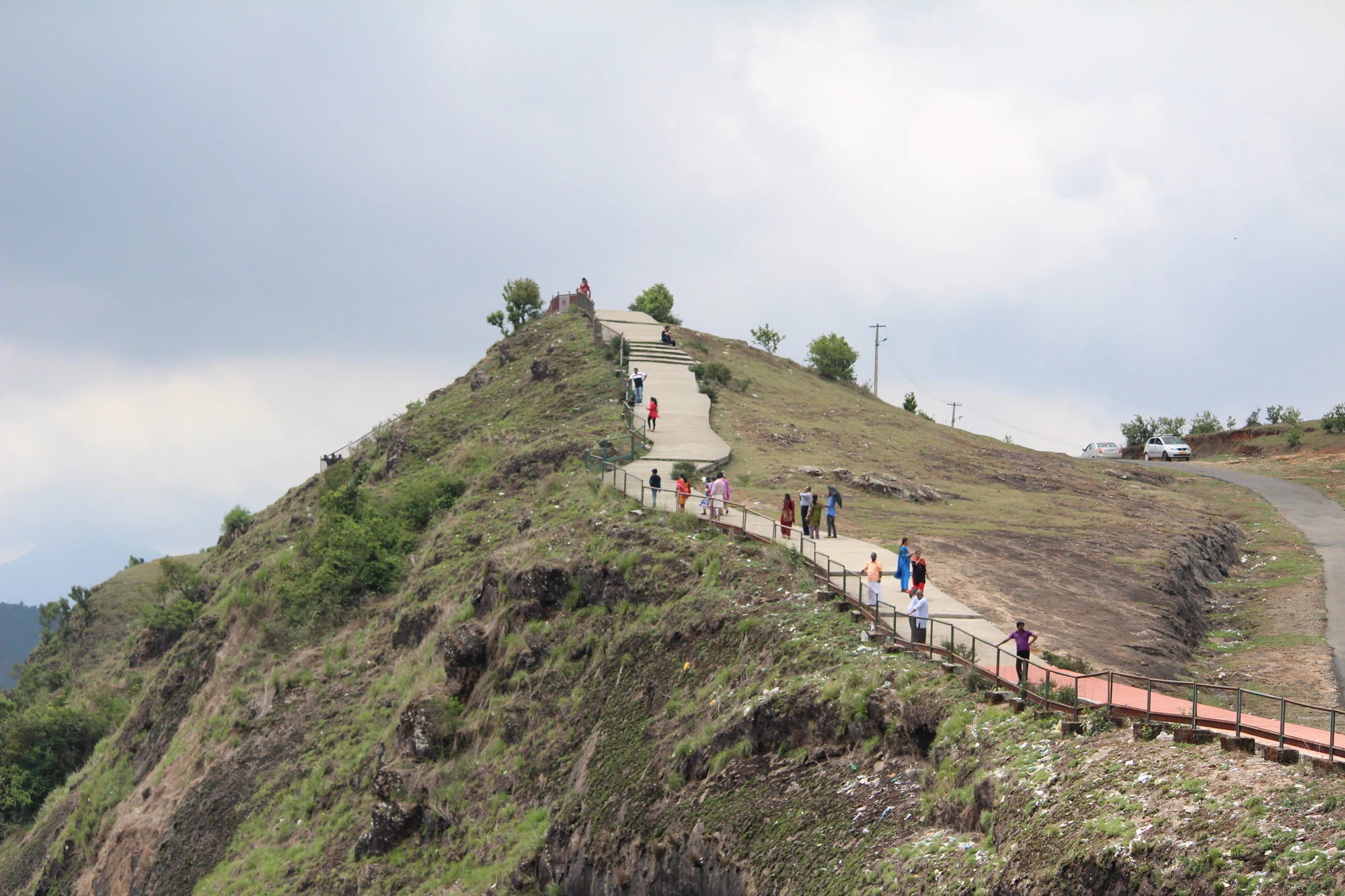 Visitors follow steps and metal-railed sections across Parunthumpara’s grassy viewpoint slope