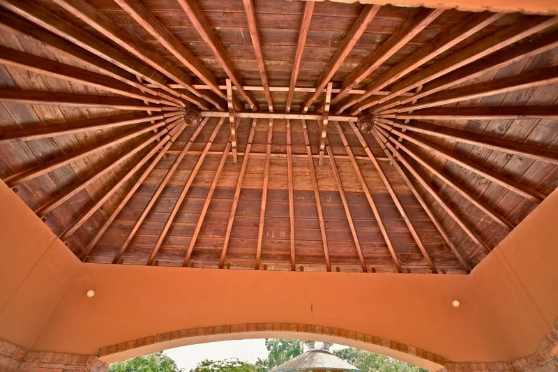 Wooden rafters form repeated lines and fan towards the corners beneath the Pazhassi memorial pavilion’s tiled roof.
