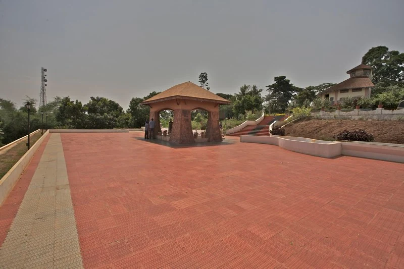 The low Pazhassi memorial pavilion stands in a broad paved court, with steps rising towards a separate building.