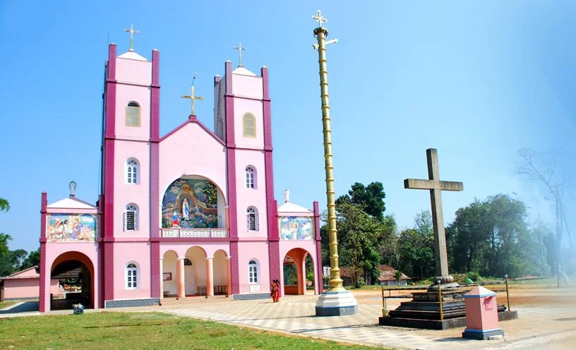 An archival view shows Pallikkunnu’s pink twin-towered façade, golden flagstaff and freestanding stone cross.