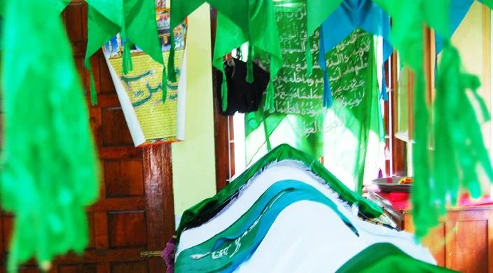 Green fabric hangs around a cloth-covered tomb inside Varambetta’s timber-posted maqaam.