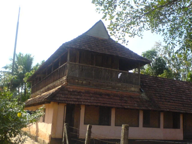 A cream-coloured building with a long tiled roof stands in the Pandalam palace setting.