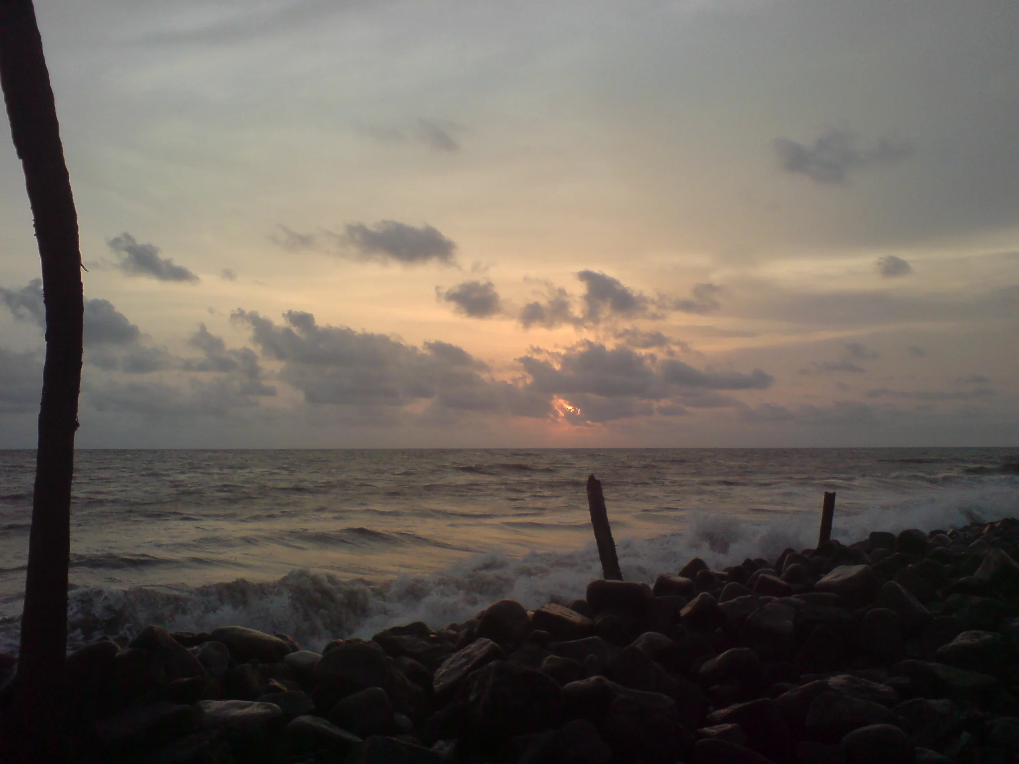 The low sun glows above the sea behind dark rock protection on the Nattika coast.