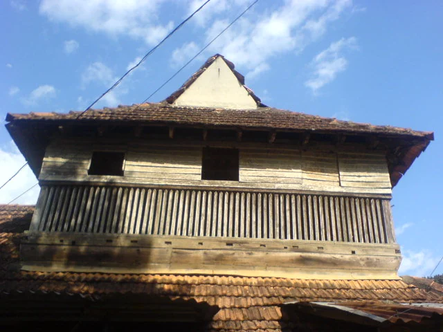 A projecting timber balcony and tiled eaves form part of a Pandalam palace building.