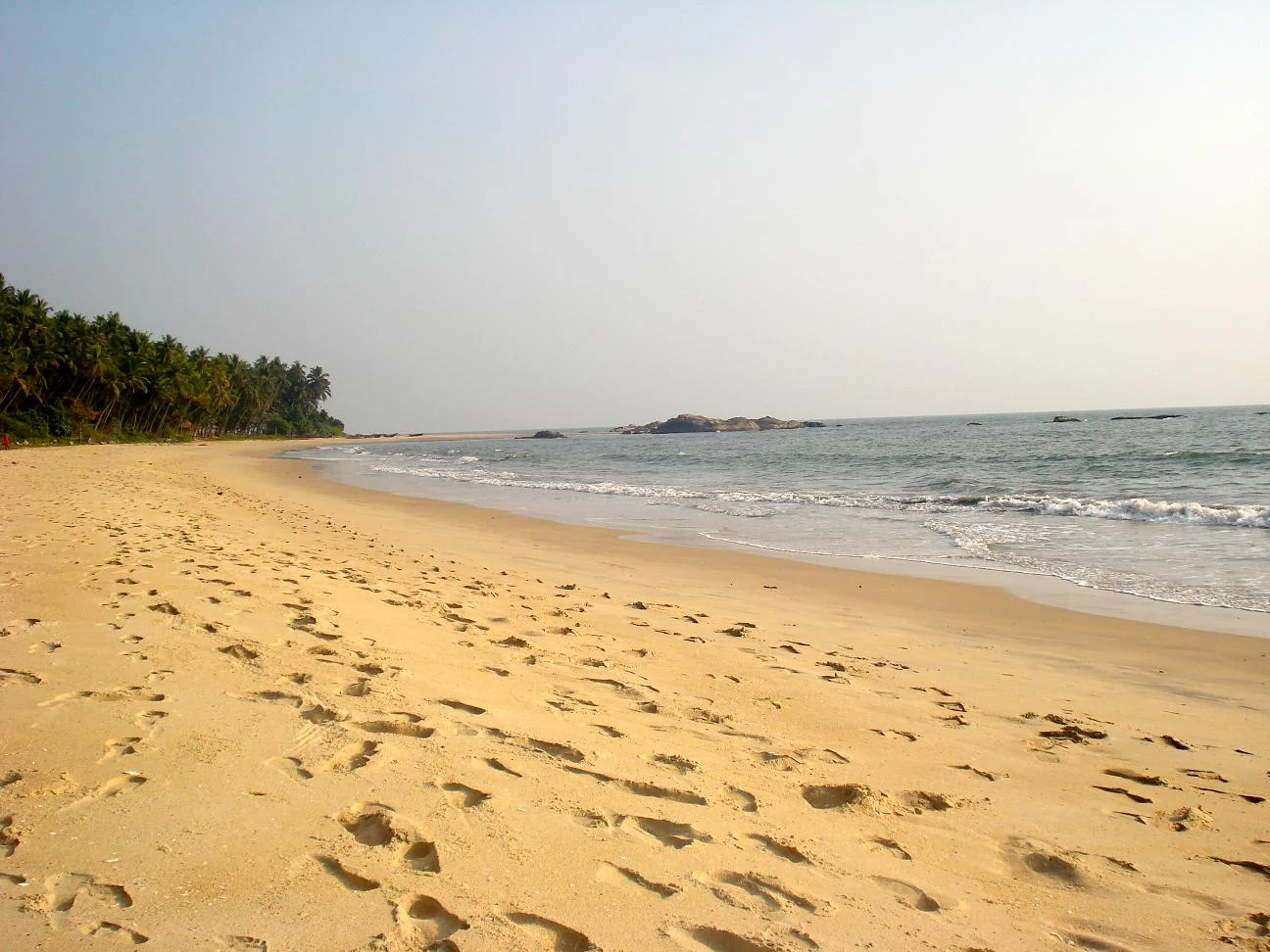 Footprints cross the open sand at Kizhunna, with low dark rocks and the sea beyond.