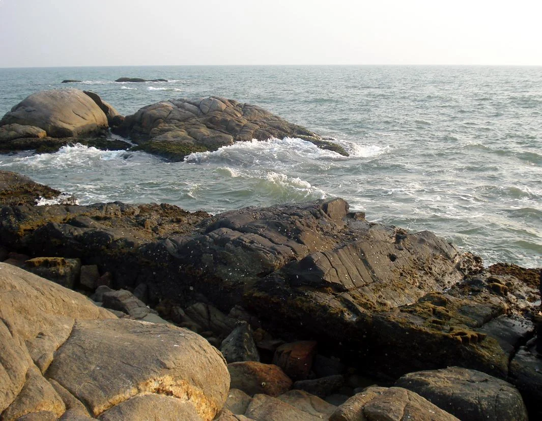 White surf breaks around rounded dark rocks at Kizhunna Beach.