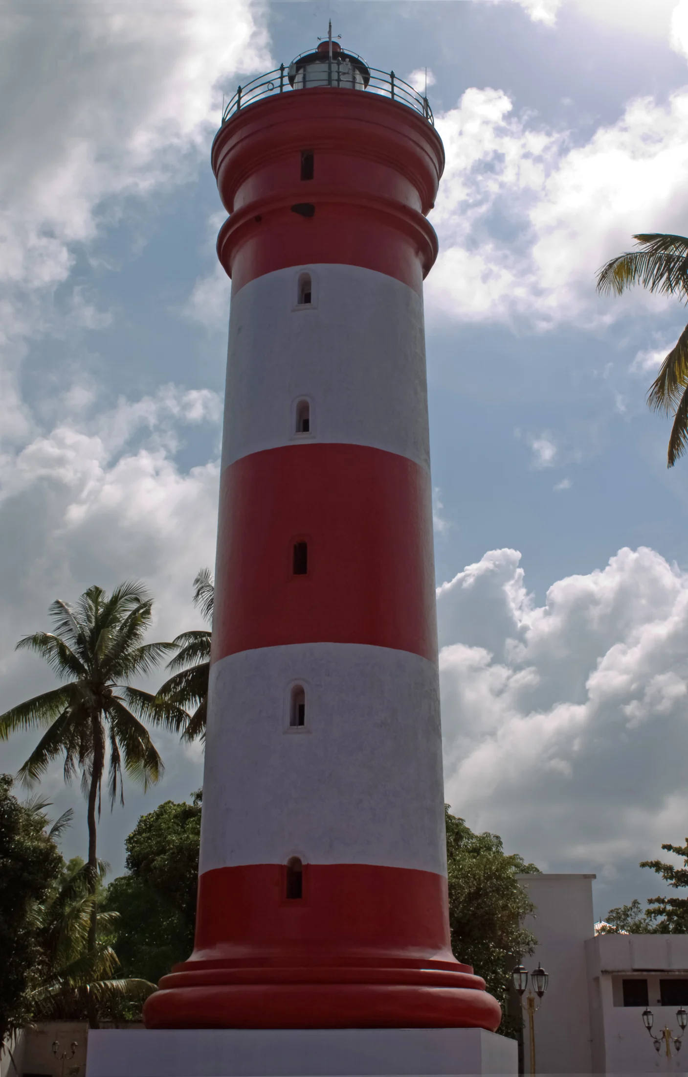 The red-and-white cylindrical lighthouse rises above its base buildings and surrounding palms.