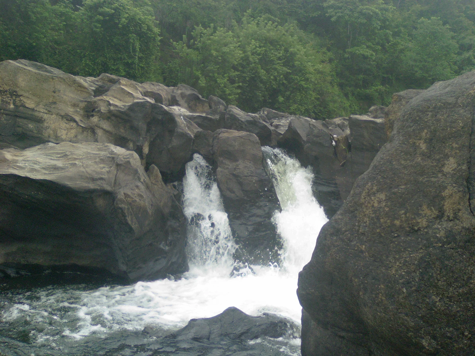 Several white chutes descend through dark rock at Perunthenaruvi, with green vegetation above.