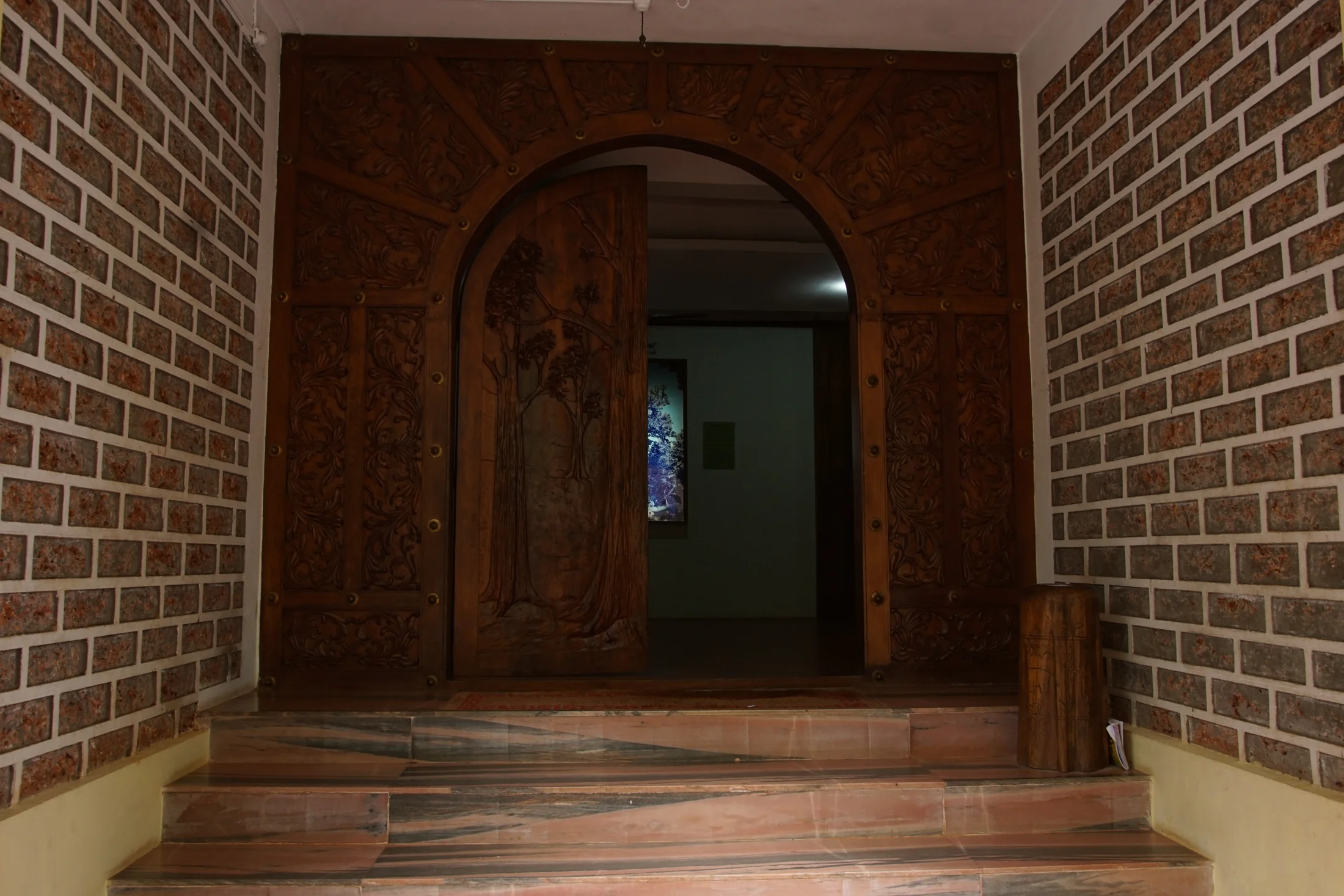 A carved timber arch frames the museum doorway above stone steps, with tree forms on the door panel.