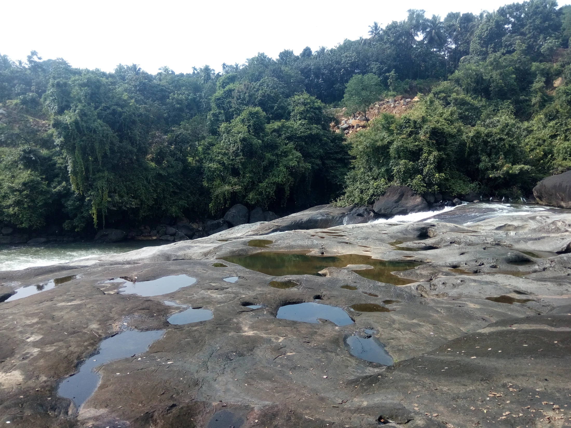 Rounded water-filled depressions lie in Arippara’s broad grey rock surface beside the flowing channel.