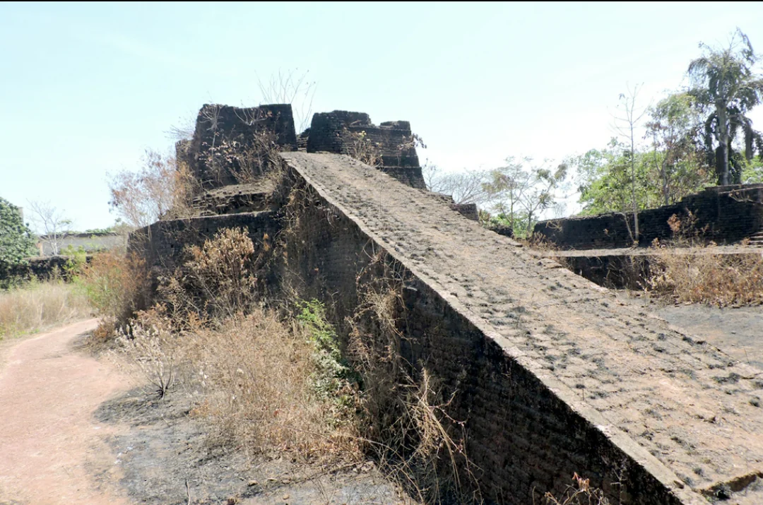 A broad ramp rises towards Hosdurg Fort’s rounded bastion, with exposed stonework and vegetation alongside.