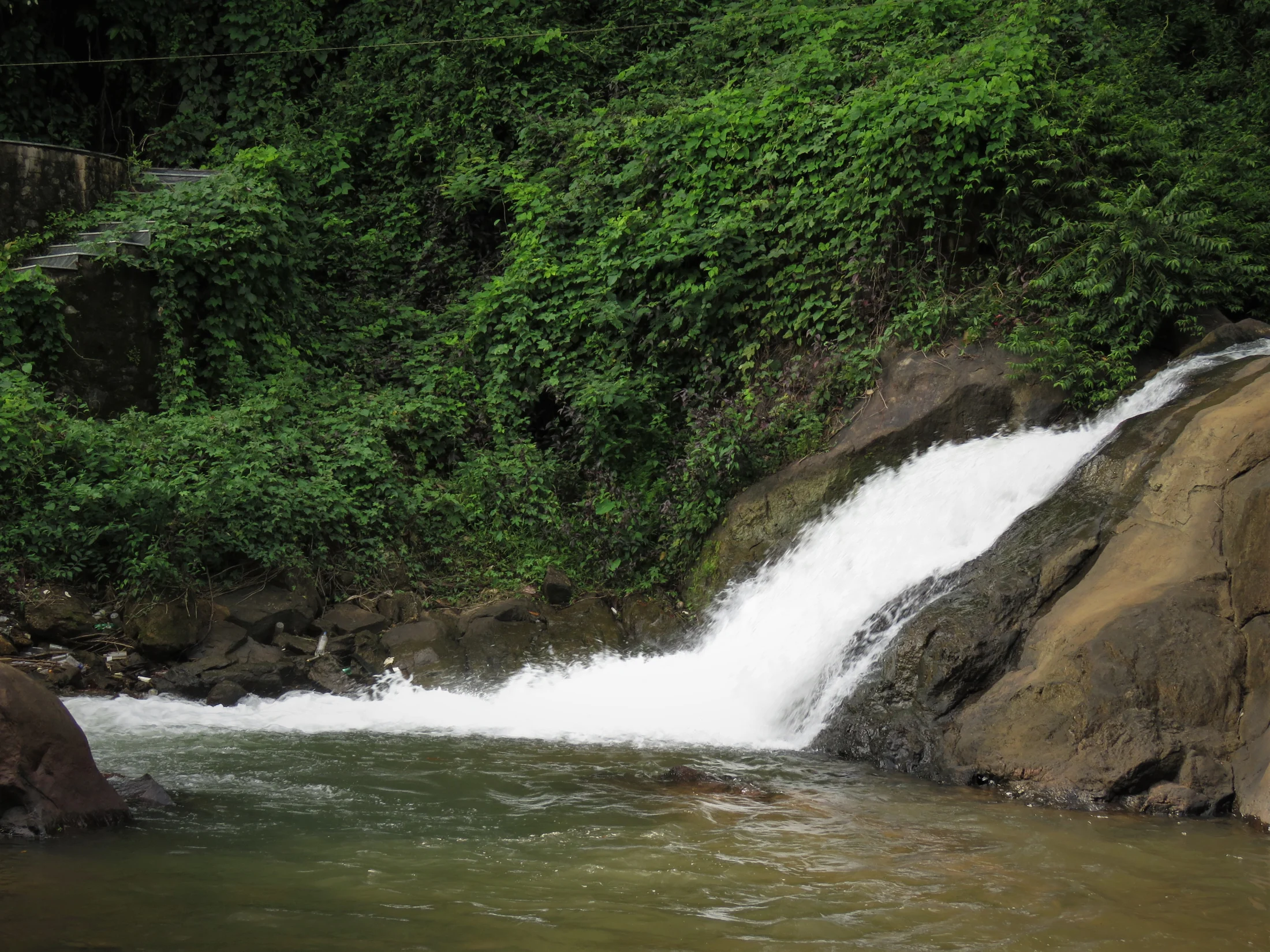 A concentrated chute of white water drops over dark rock into a pool at Aruvikkuzhi.