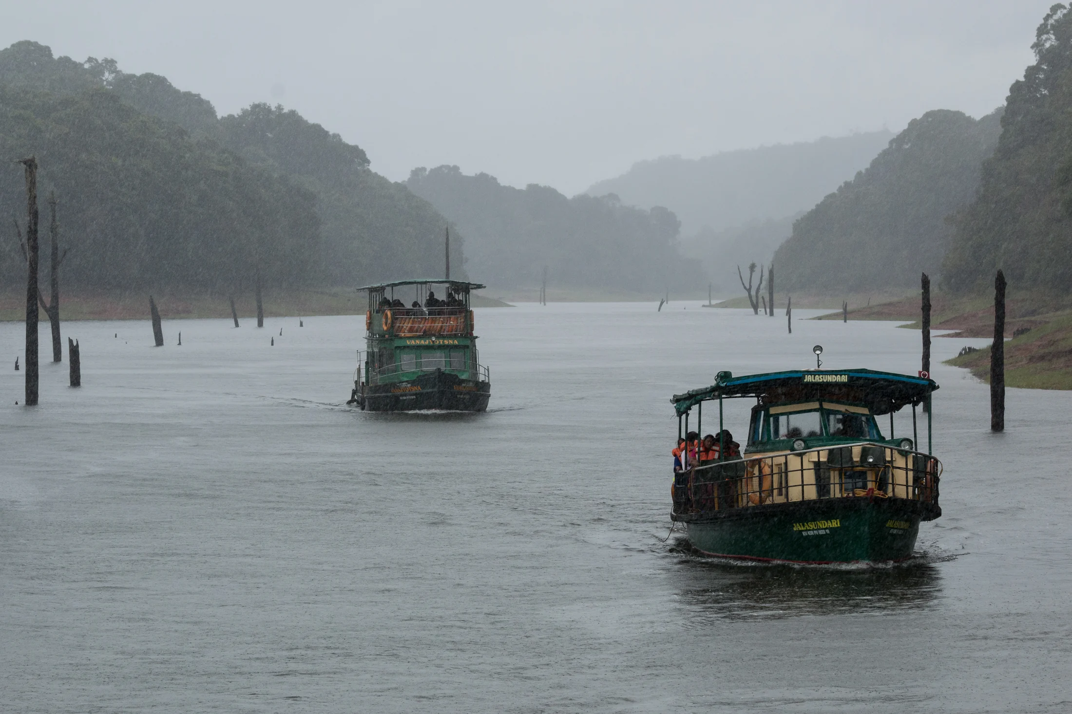 Passengers wear orange lifejackets on a covered Periyar boat during wet weather.