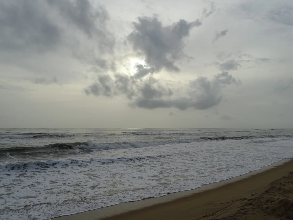 Waves reach a broad sandy shore beneath a cloudy sky at Kanhangad.