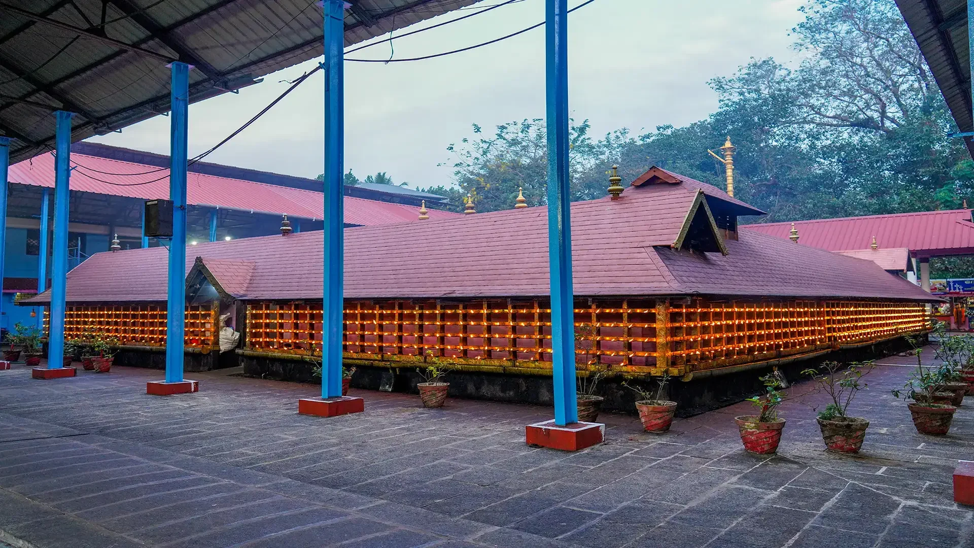 Rows of lamps line a tiled temple enclosure at Malayalapuzha, with blue-painted columns below.