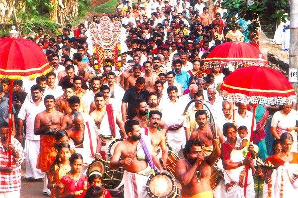 Drummers and a procession gather beneath red ceremonial umbrellas at Malayalapuzha.