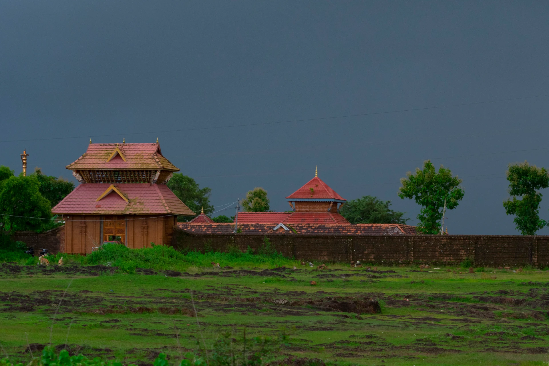 Vadukunda’s walled enclosure beneath a dark sky, with wet grass in the foreground.