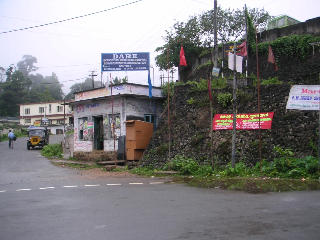 Peermade’s town junction, with vehicles, signs and mist beyond the street.