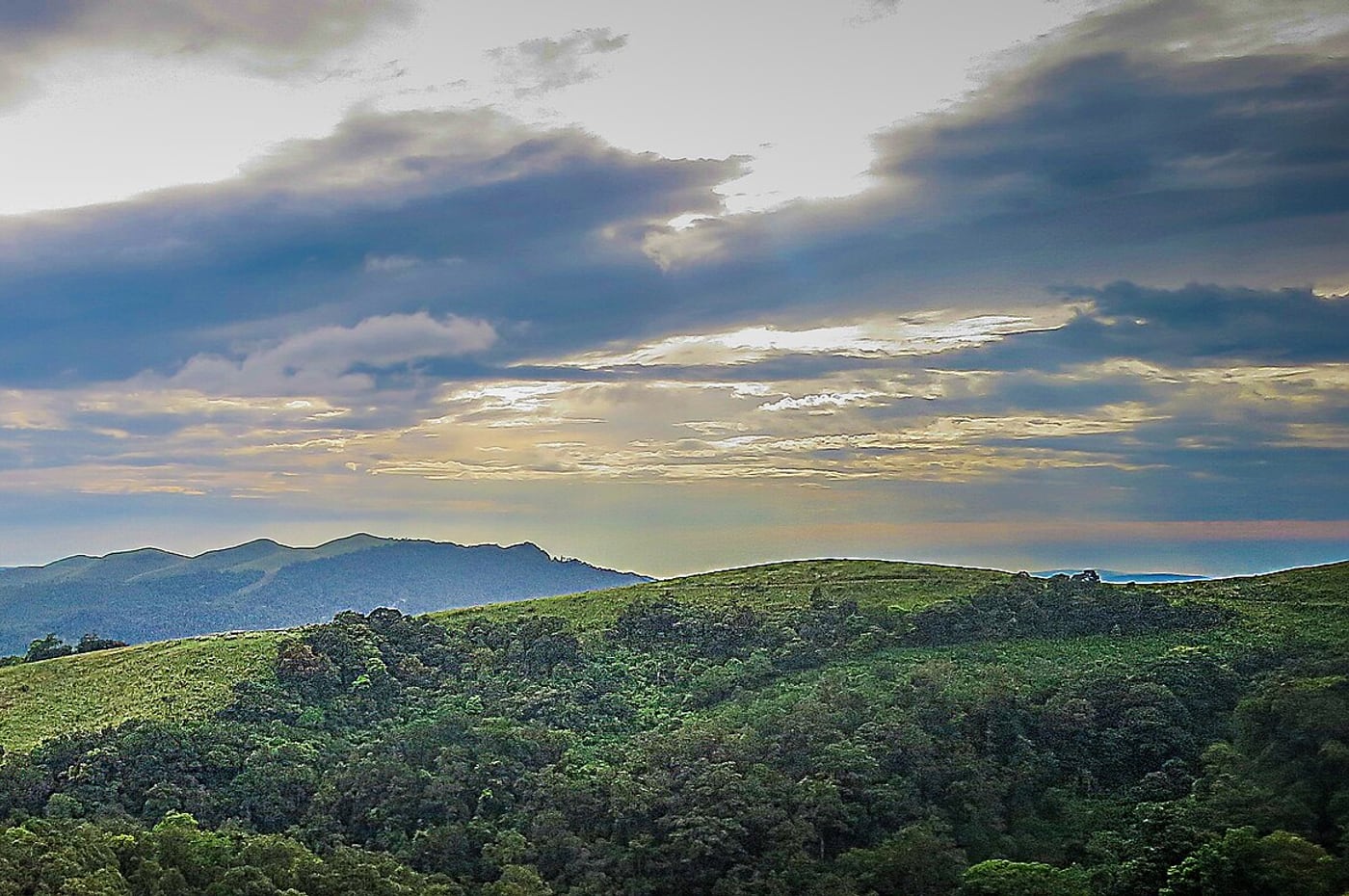 Sunlight breaking through cloud above the grass ridges and forested folds of Gavi